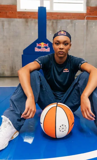 Hannah Hidalgo sitting on a blue court in a Red Bull cap with a basketball at her feet
